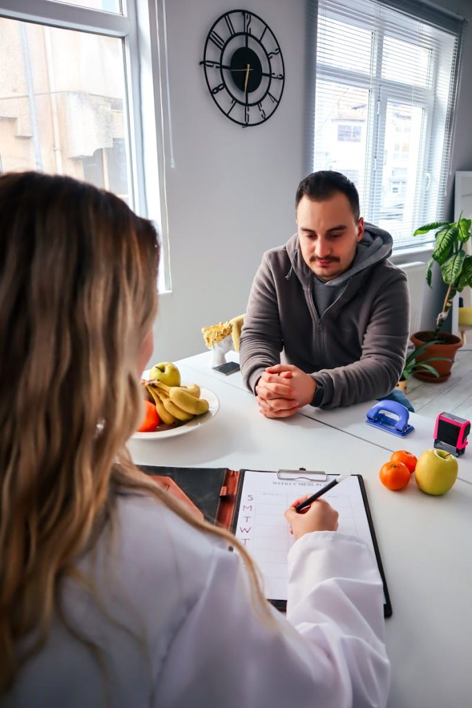 A male consulting with a dietitian during a health session, indoors with fruits.