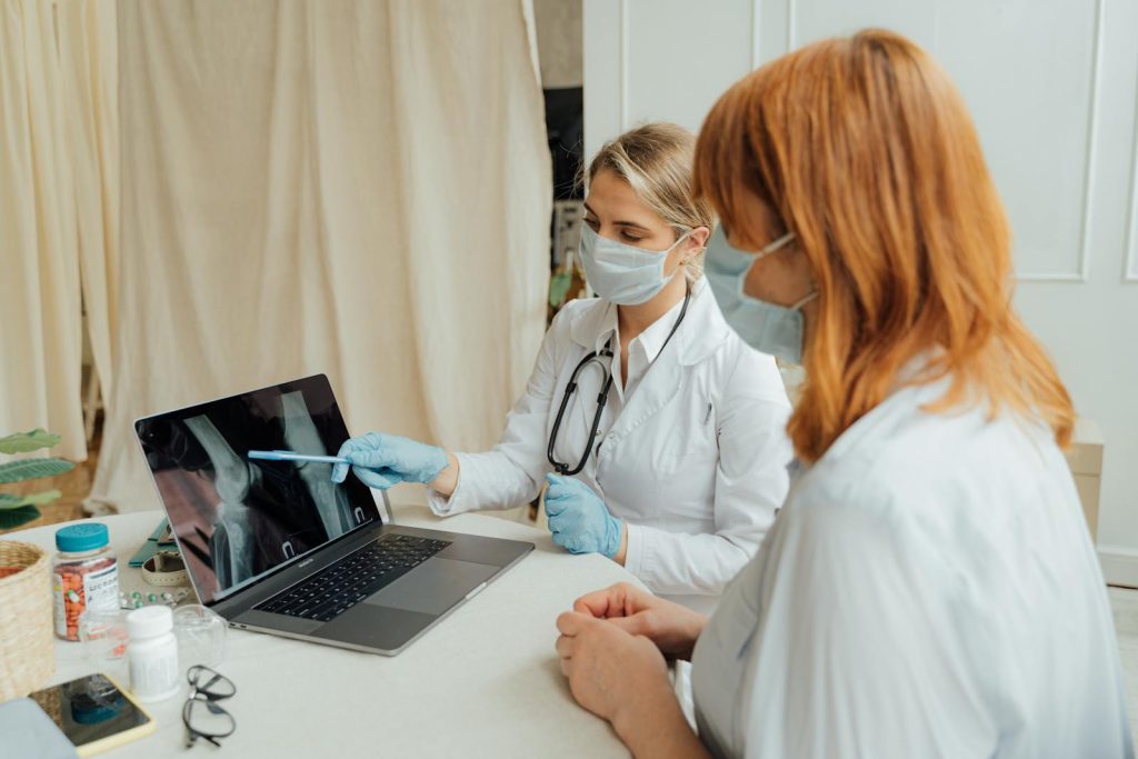 Doctor explains X-ray results to patient using a laptop in a clinic setting.
